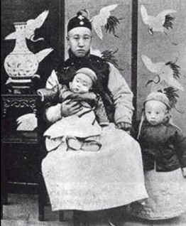 On her death-bed in 1908, Cixi made her two-year-old great-nephew, Puyi (standing), the next emperor, and his father, Zaifeng (seated holding Puyi's brother), the Regent.