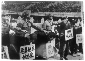 The people being exhibited carry plaques announcing that they are 'landlords' and 'spies'.